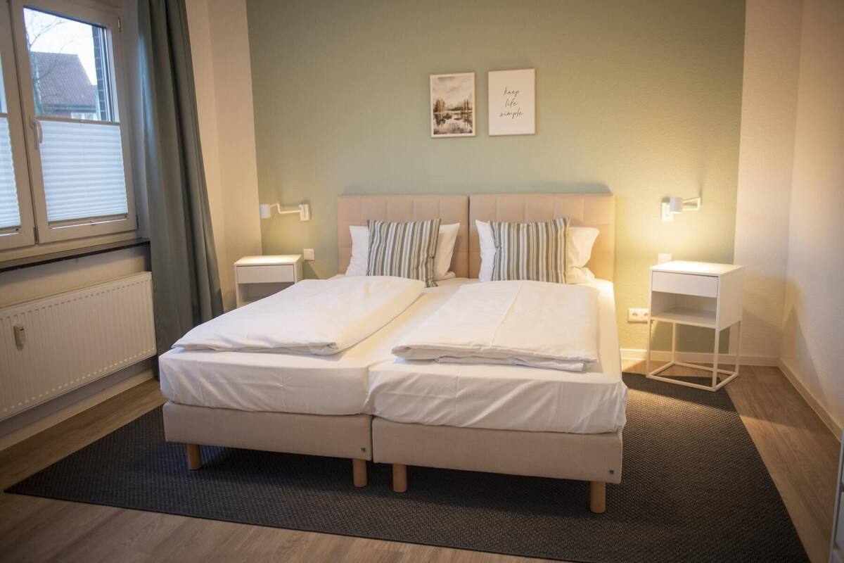 A double bed with two pillows, a bedside table, a wall-mounted lamp, and a framed picture on the wall.