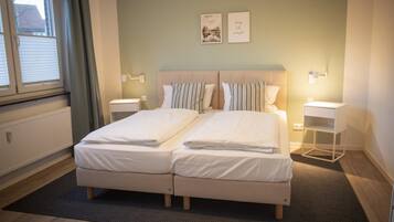 A double bed with two pillows, a bedside table, a wall-mounted lamp, and a framed picture on the wall.