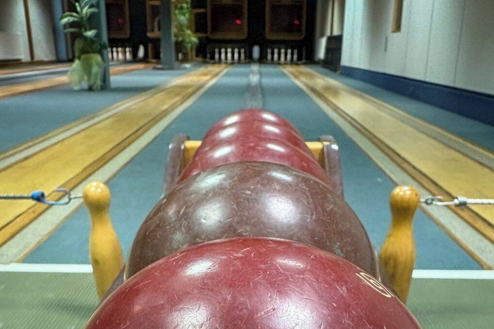 Una pista de bolos con una bola de boliche marrón y roja en primer plano.