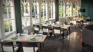 Een restaurant met grote rondboogvensters, houten tafels en stoelen.