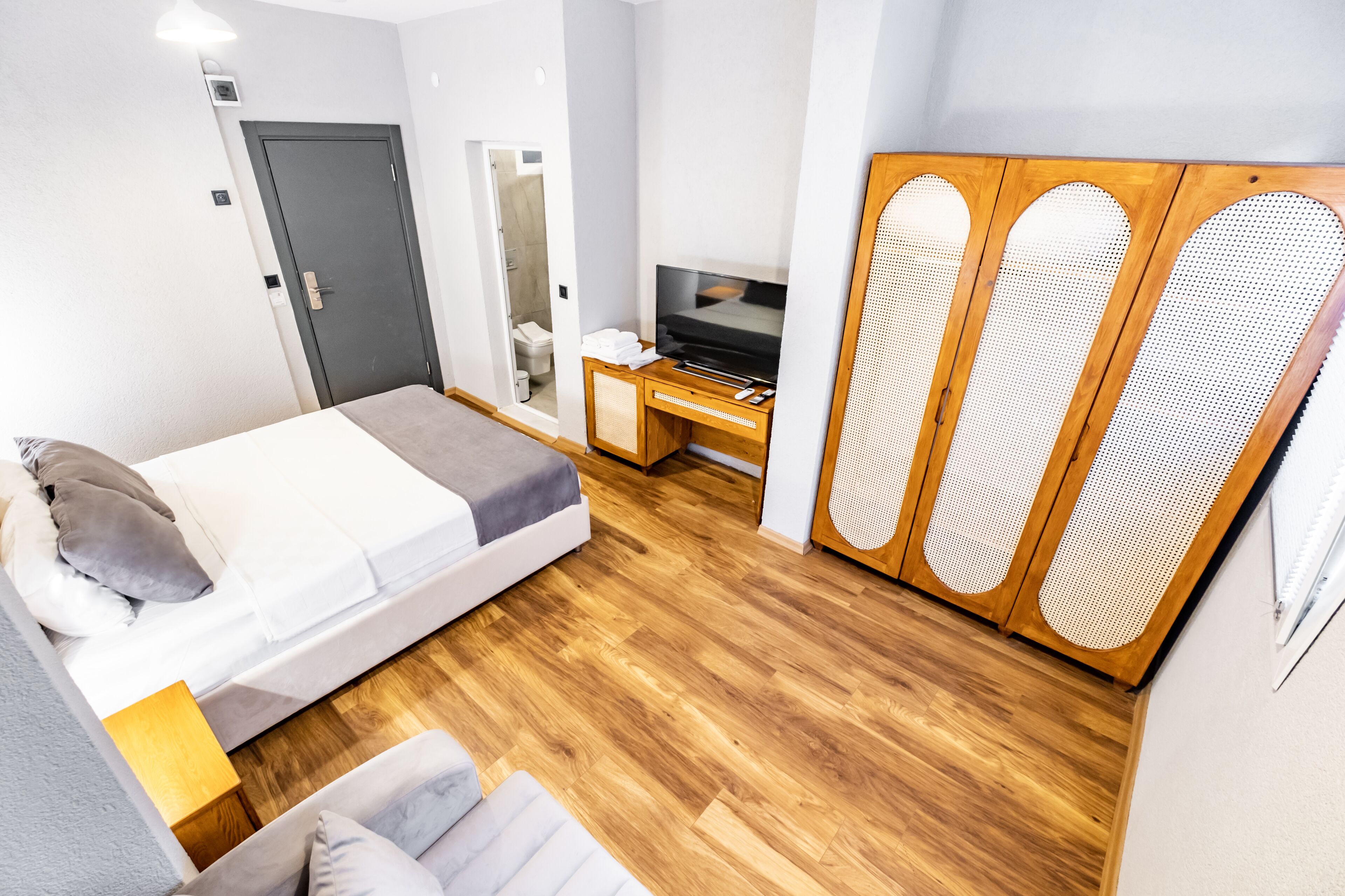 A modern bedroom with a bed, a TV, a wooden wardrobe, and a shower area.