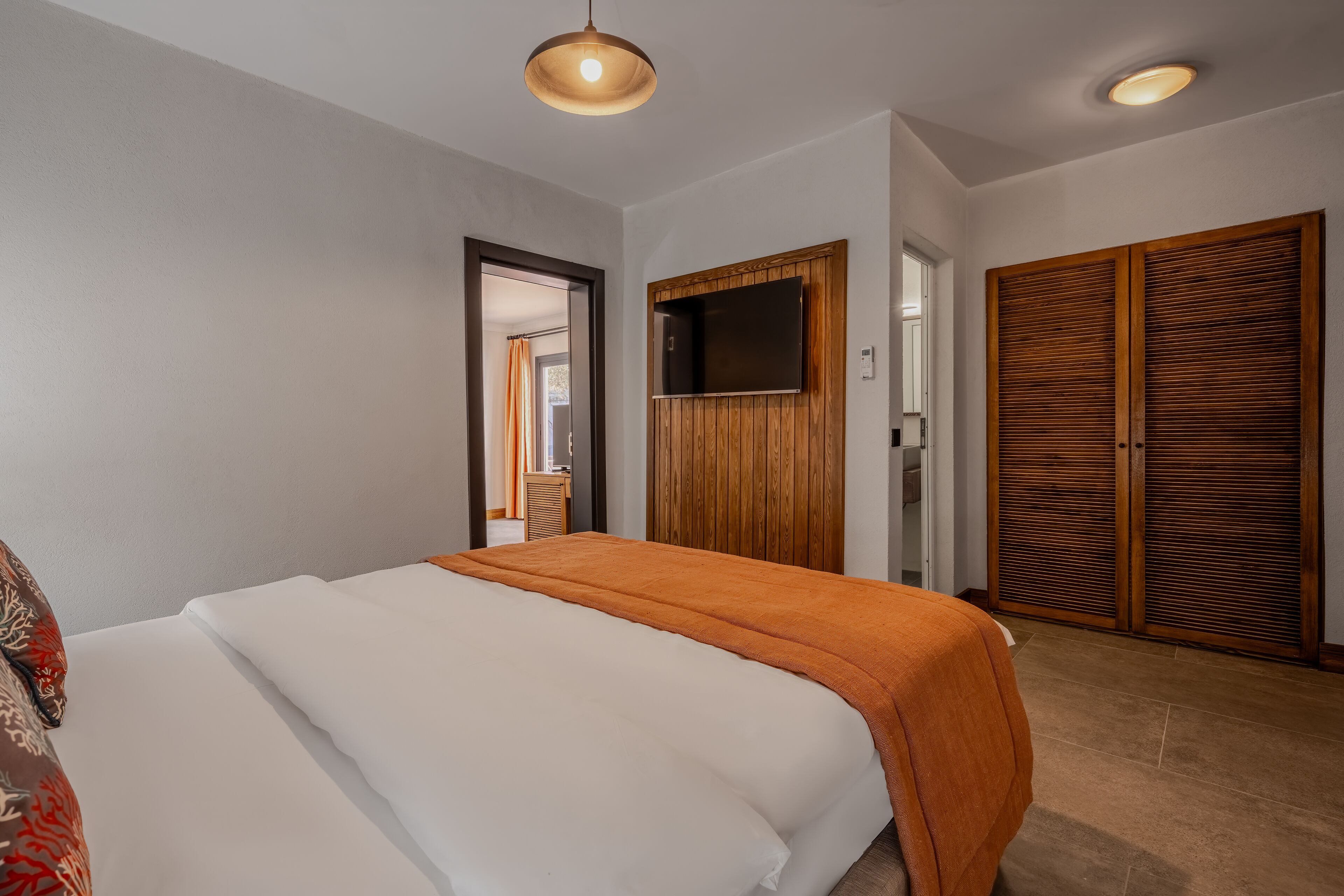 Une chambre d’hôtel avec un lit, un téléviseur fixé au mur et une armoire en bois.