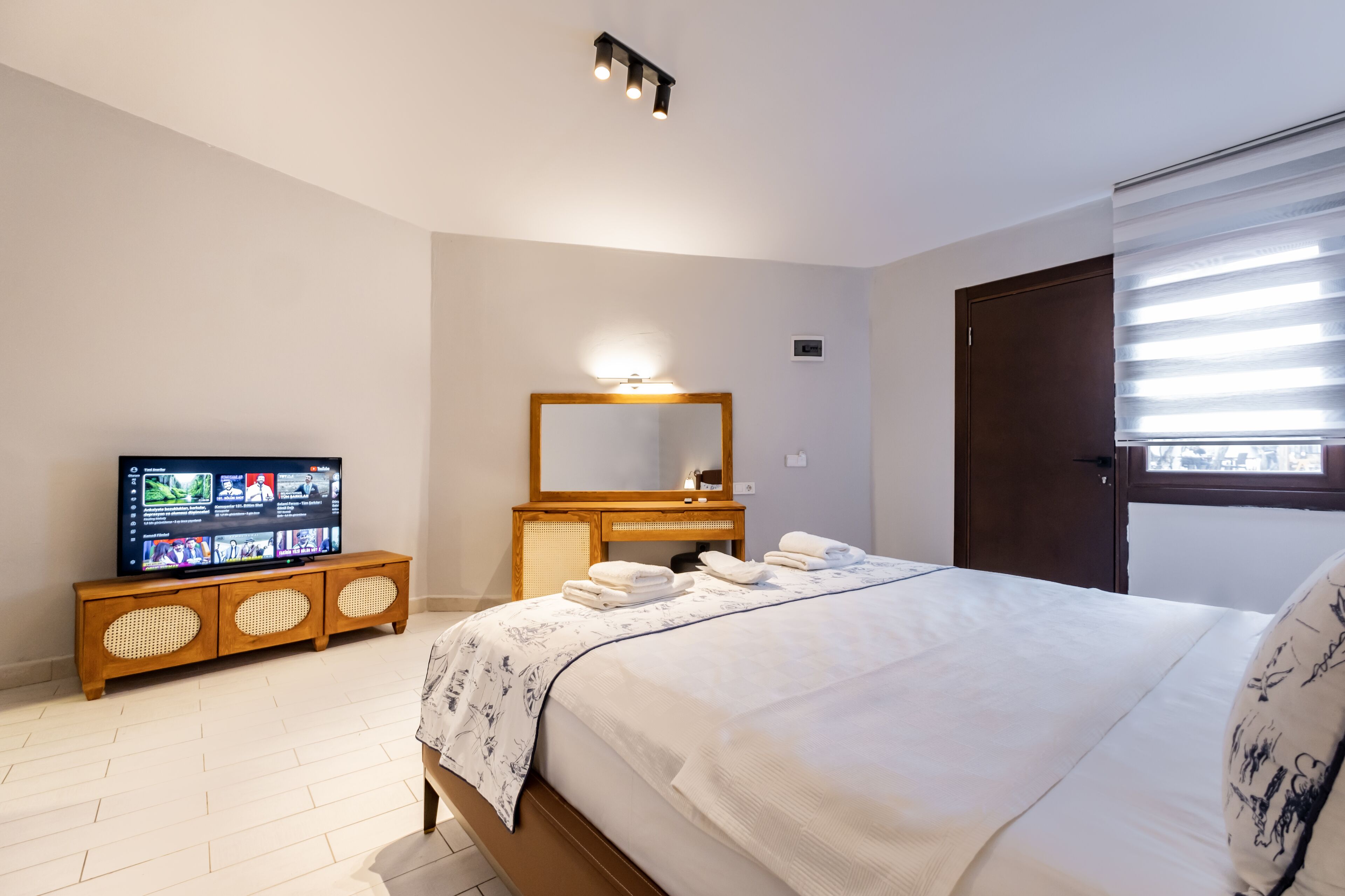 Un dormitorio con una cama, un televisor sobre un mueble de madera, un espejo y una ventana con persianas.