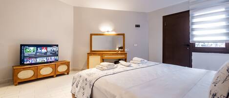 Un dormitorio con una cama, un televisor sobre un mueble de madera, un espejo y una ventana con persianas.