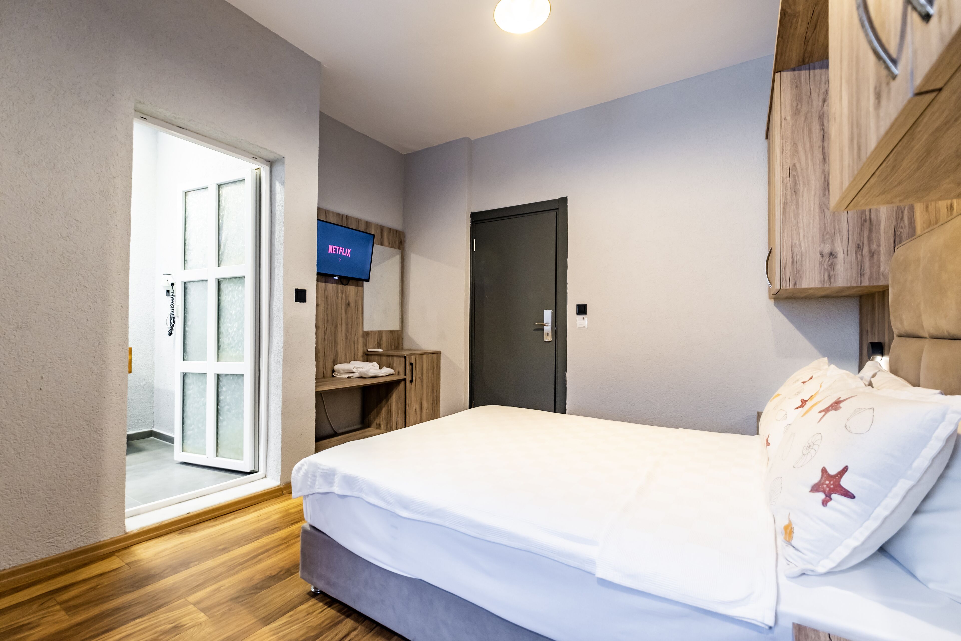 Une chambre d’hôtel comprenant un lit, un téléviseur fixé au mur, une armoire en bois et une porte donnant accès à une salle de bain.