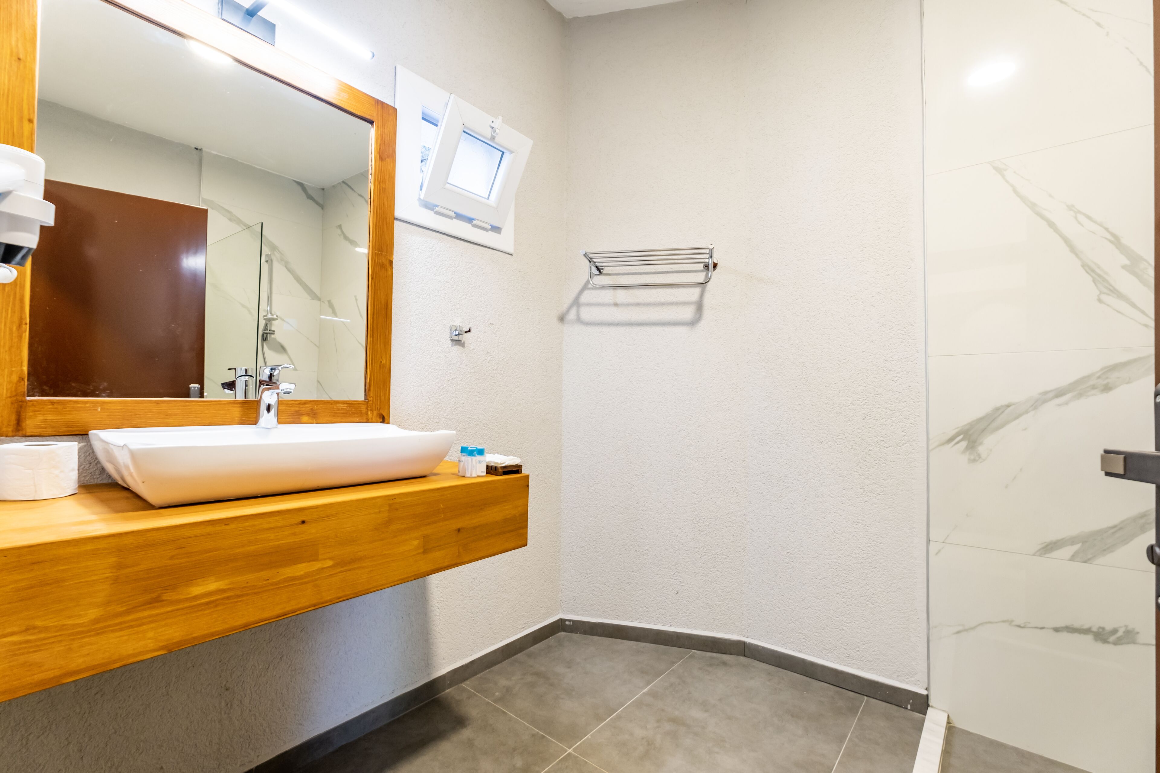 Un baño moderno con tocador de madera, un espejo grande, un lavabo blanco y una cabina de ducha con paredes de vidrio.