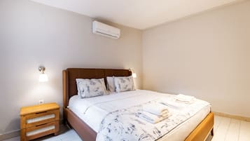 Una cama bien hecha con una colcha floral, una mesita de noche de madera con cajones y un aire acondicionado de pared.