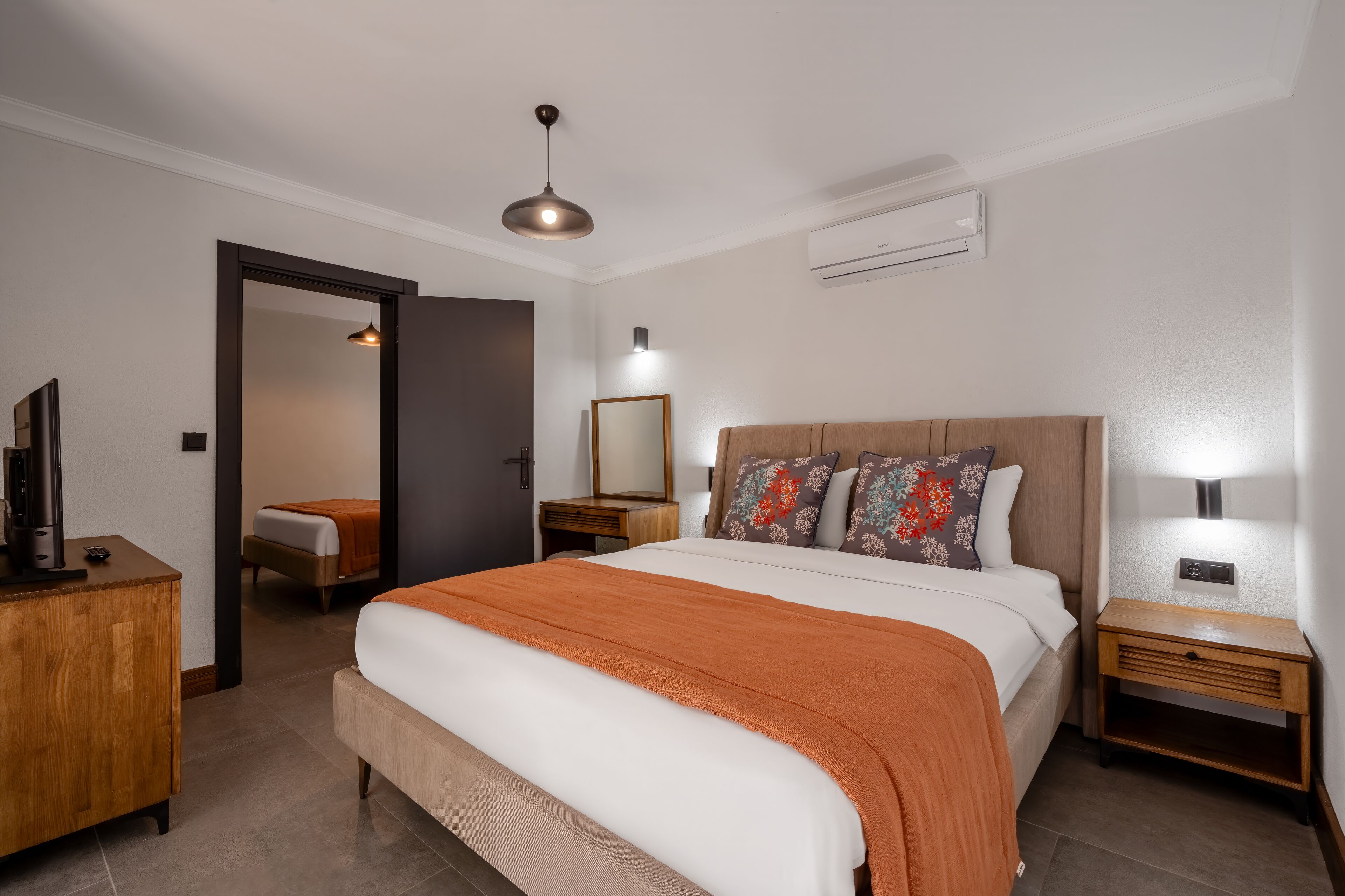 Una habitación de hotel con una cama grande, mesitas de noche, un armario, un espejo y una lámpara en el techo.