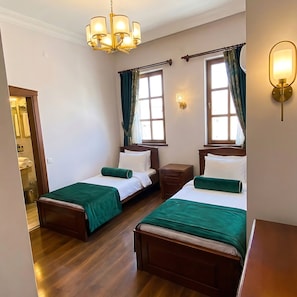 Een hotelkamer met twee bedden, houten vloeren, een kroonluchter en uitzicht door ramen.