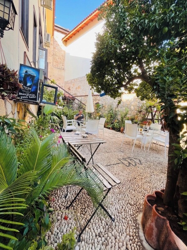 An outdoor patio with white chairs and tables, surrounded by pebbles and plants.
