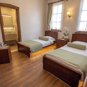 Een hotelkamer met twee bedden, een houten vloer, een badkamer met spiegel en wastafel, en een raam met gordijnen.