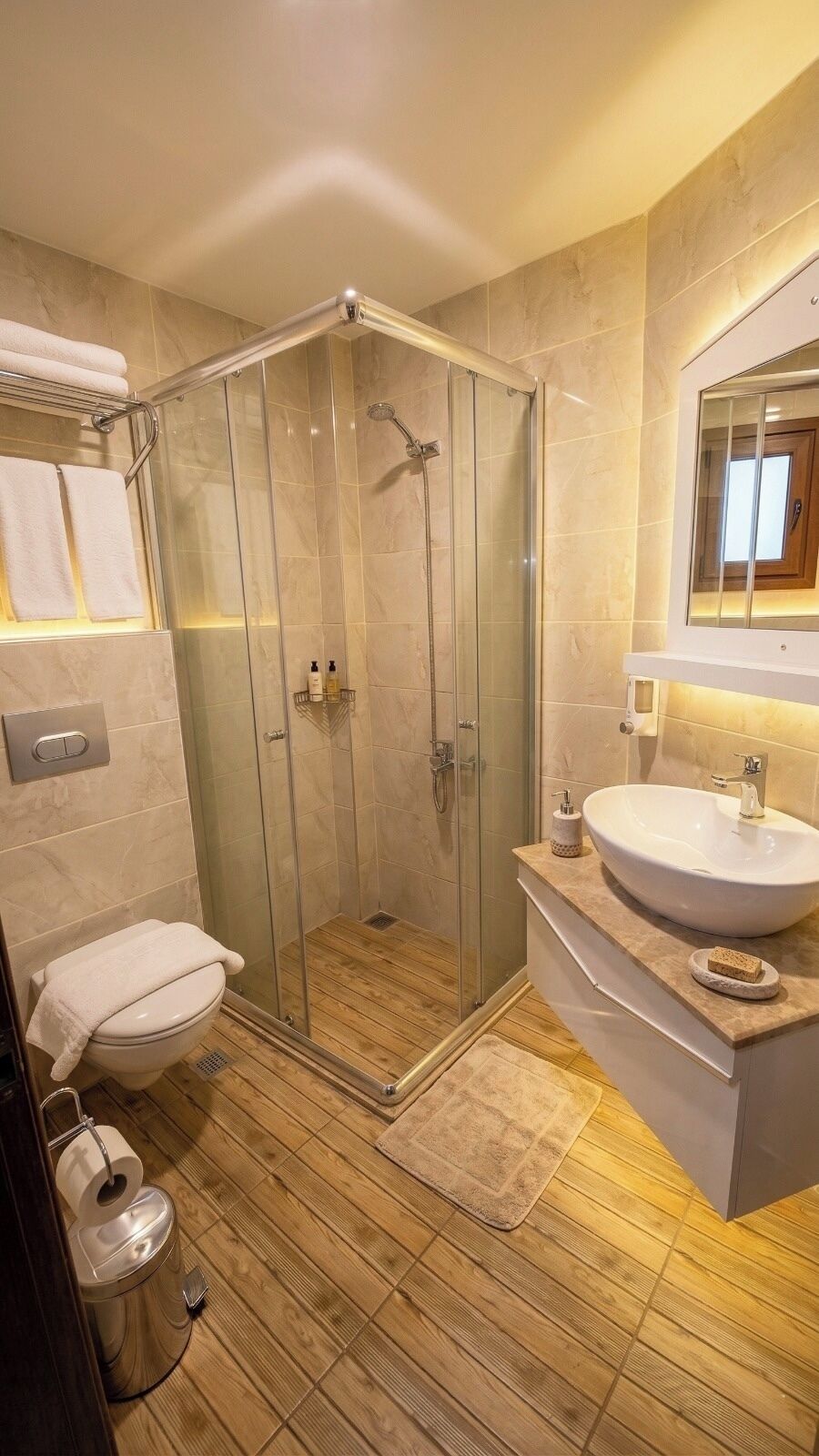 Een moderne badkamer met een glazen douchecabine, een toilet, een wastafel met spiegel, en een houten vloer.