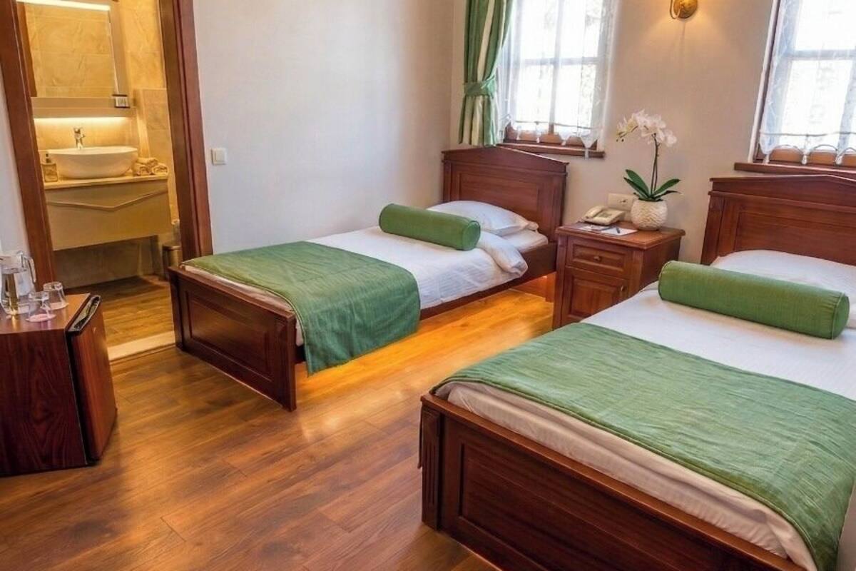 A hotel room with two wooden beds, a wooden nightstand, a small table, a mirror, a chandelier, and a window with curtains.