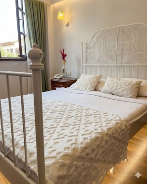 Een bed met een wit hoofdeinde, een nachtkastje met een lamp en een raam met gordijnen.