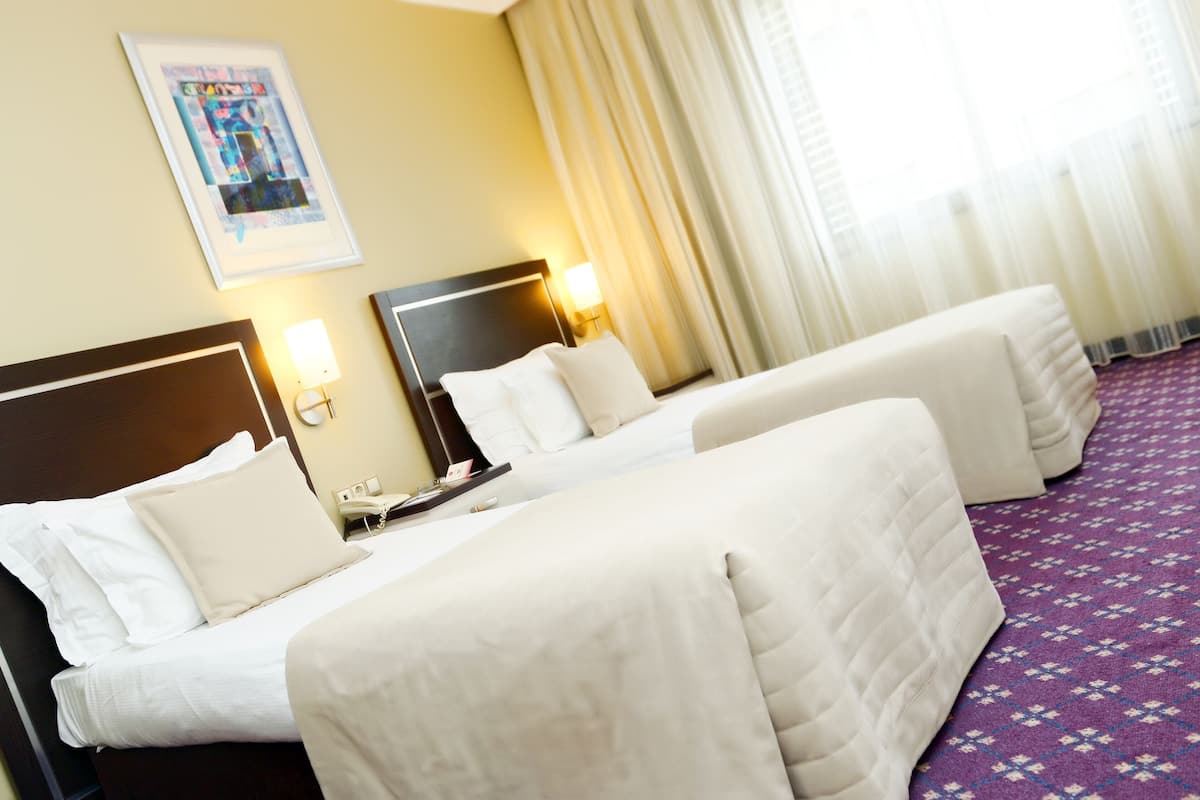 A hotel room with two beds, a nightstand, a lamp, and a poster on the wall.