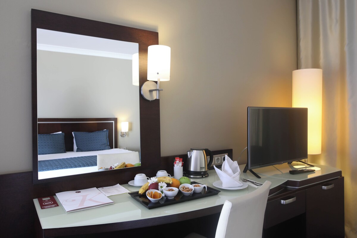 Une chambre d’hôtel avec un lit, un bureau équipé d’un ordinateur, un plateau avec des articles pour le petit-déjeuner et un grand miroir.