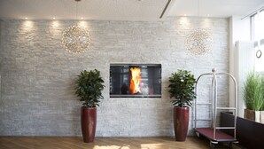 A modern lobby with a stone wall, a fireplace, and two large potted plants. - City Aparthotel Muenchen (Muenchen)