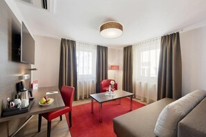 Une chambre d’hôtel comprenant un coin repas, un canapé, une télévision et une lampe.