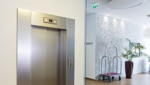 A modern elevator with a metallic finish, a reception area with a stone wall, and a potted plant. - City Aparthotel Muenchen (Muenchen)