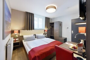 Une chambre d’hôtel comprenant un lit, des tables de chevet, un bureau avec une chaise, une douche et une armoire.