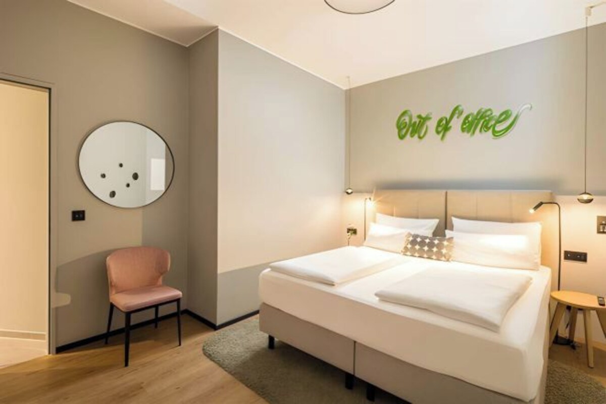 A hotel room with a bed, a chair, and a wall-mounted mirror.