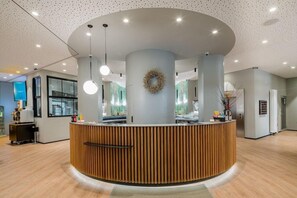 Un espace d’accueil doté d’un comptoir de réception en bois, d’un plafond à motifs circulaires et d’une guirlande décorative fixée au mur.