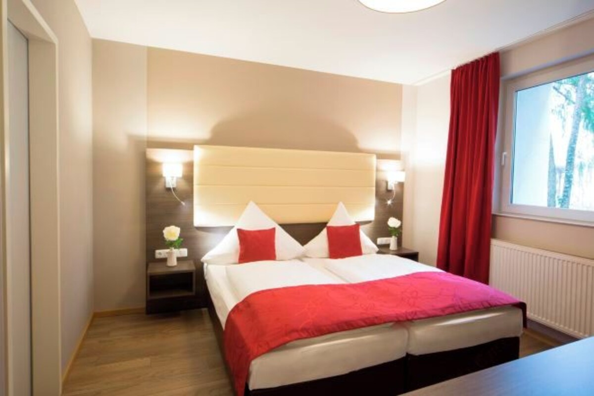 A hotel room with a bed, bedside tables, a window with curtains, and a view of trees.