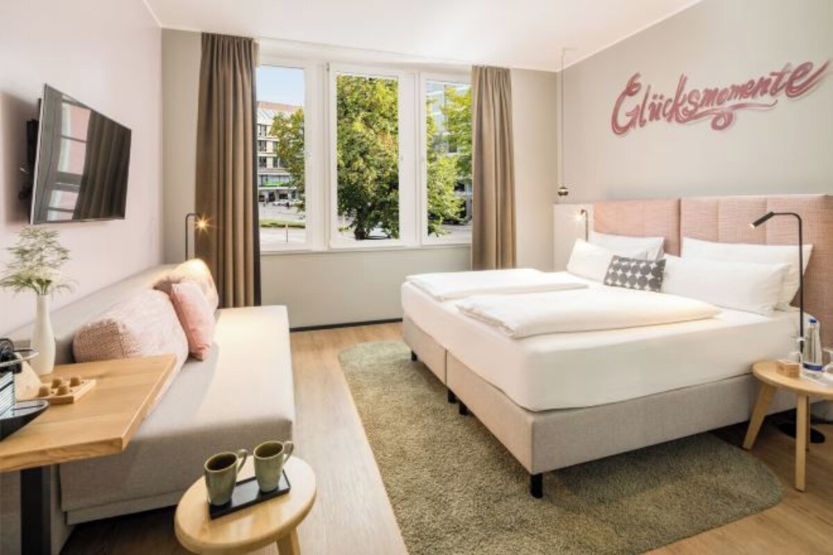 A hotel room with a bed, a sofa, a desk, and a window with curtains.