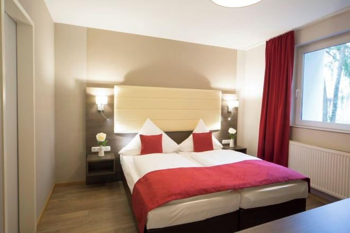 A hotel room with a bed, bedside tables, and a window with curtains.