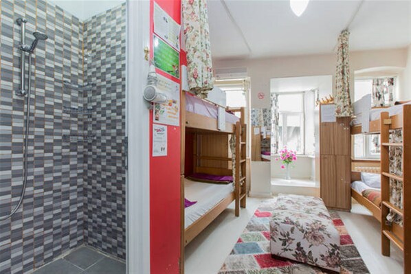 Un dormitorio con literas, ducha, ventana con cortinas y un escritorio pequeño.