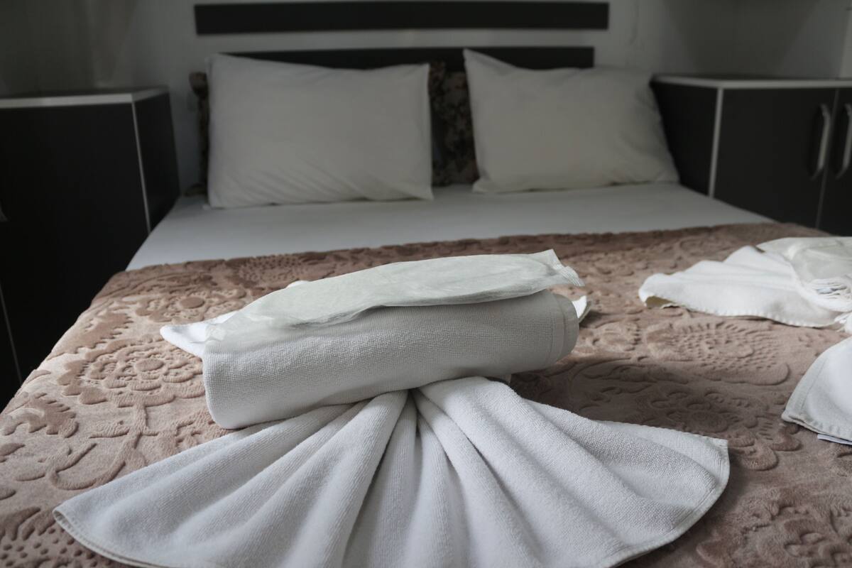 A neatly made bed with a patterned bedspread, pillows, and folded towels.