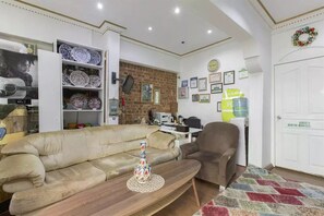 A living room with a sofa, armchair, and a table with a decorative vase. There are shelves with plates and a brick wall in the background. - Taksim Green House Hostel (Istanbul)