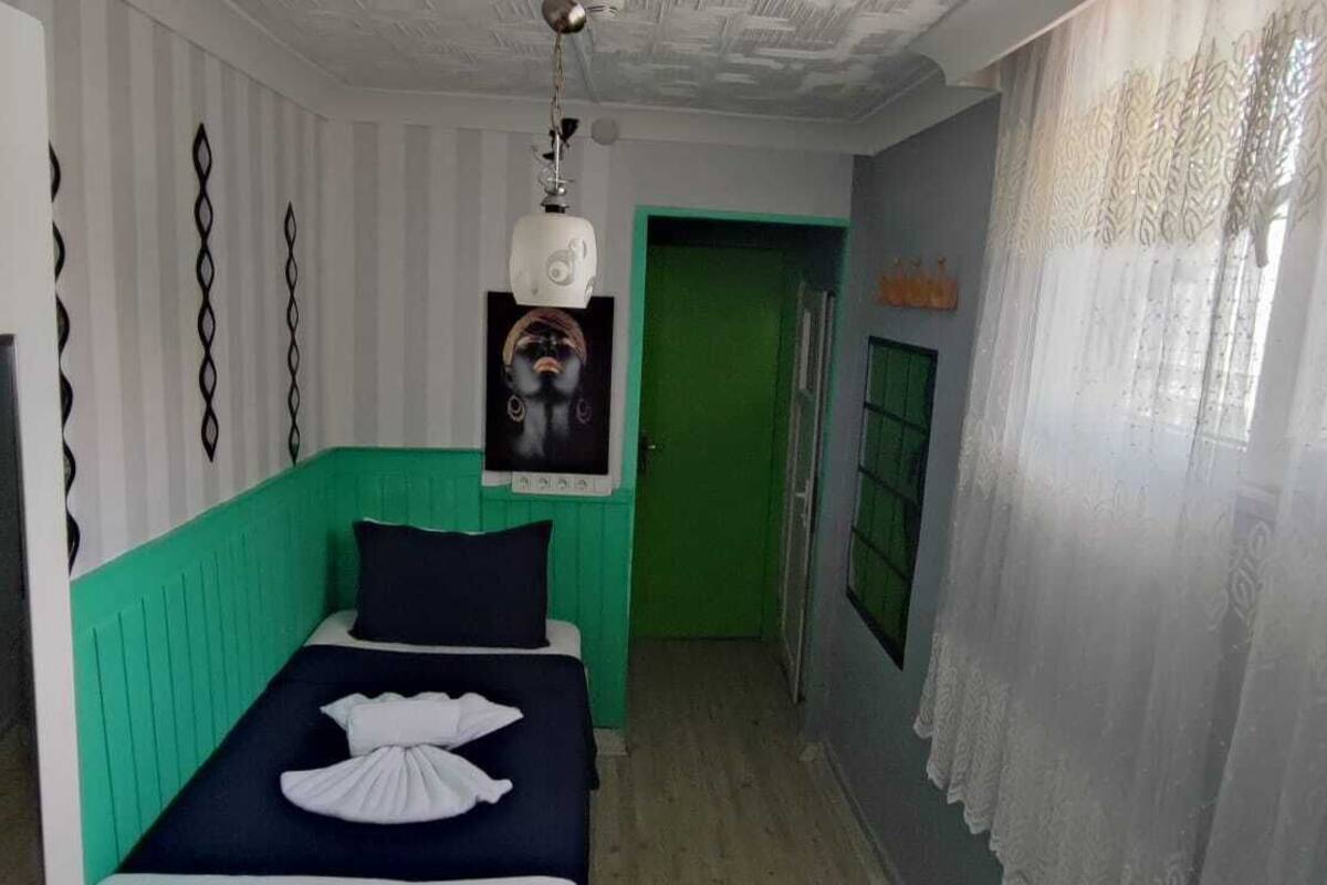A room with a bed, a green accent wall, a poster on the wall, and a window with curtains.