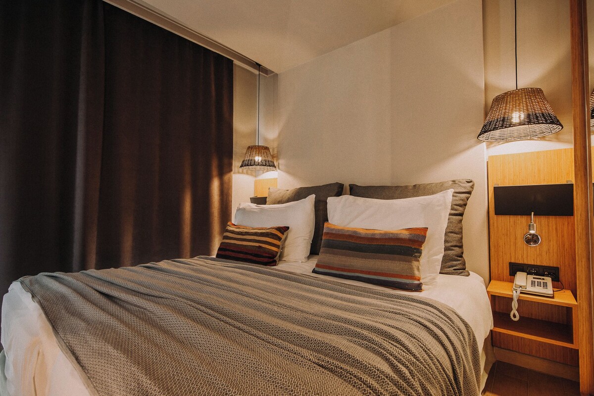 A neatly made bed with striped bedding, a bedside lamp, and a telephone on a wooden nightstand.