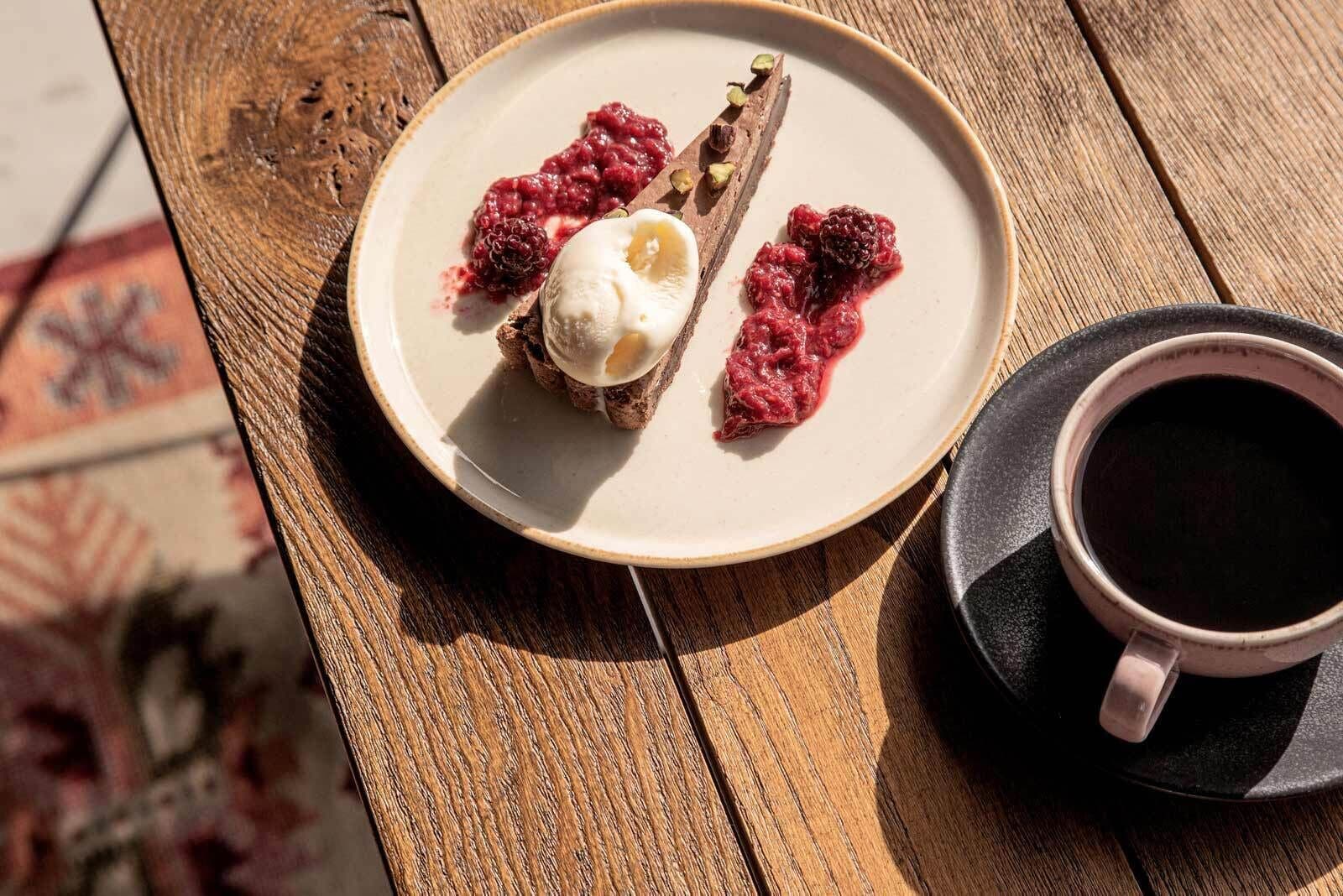 A dessert plate with berries and ice cream on a wooden table, next to a cup of coffee.