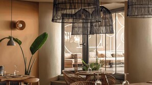 Een eethoek met rieten meubels, een ronde tafel en hangende zwarte lampen.