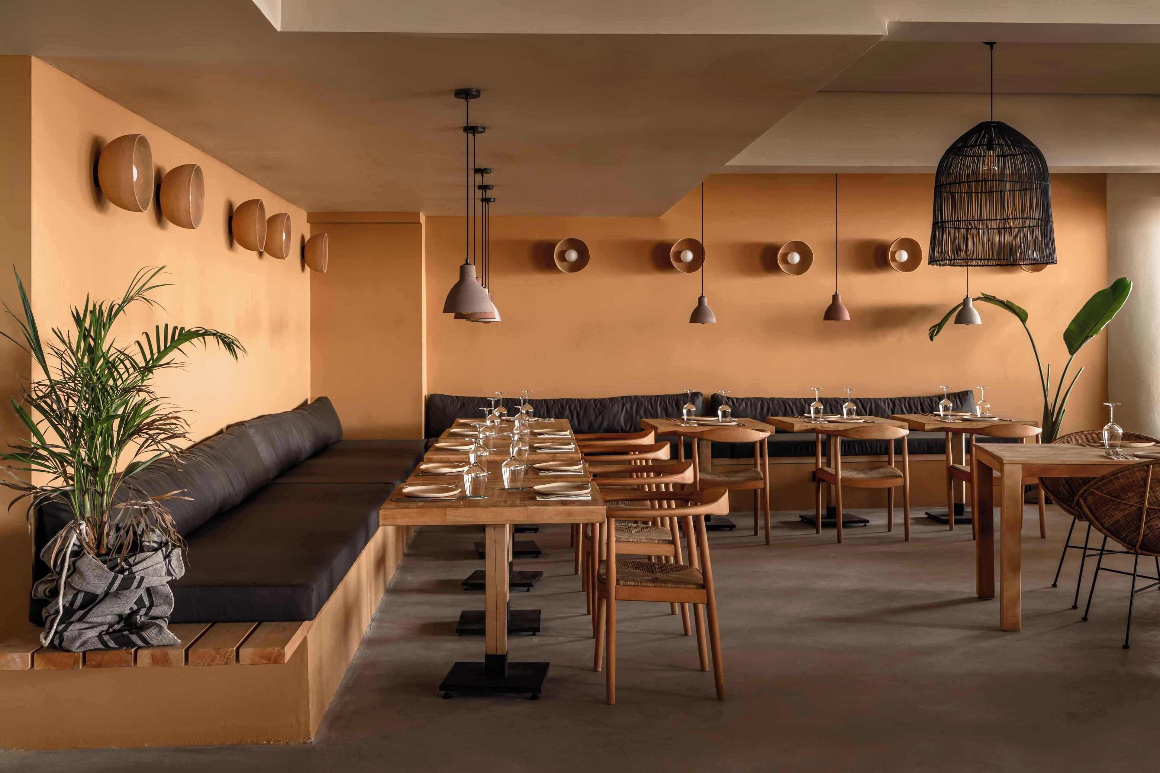 Un restaurant avec une longue table en bois, dressée pour le repas, un banc noir rembourré et des lampes suspendues.