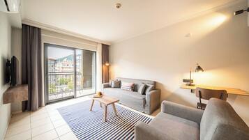 Een moderne woonkamer met een bank, fauteuil en salontafel. Er is een balkon met uitzicht op gebouwen en een berg.