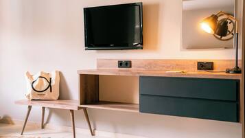 Un bagno moderno con TV a schermo piatto sopra un mobile bagno in legno, un portasciugamani e uno specchio con illuminazione integrata.