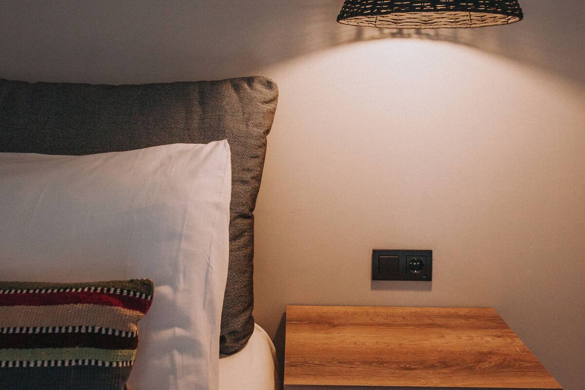 A bedroom with a bed, a bedside table, and a hanging lamp.