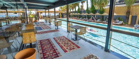 A poolside area with multiple seating arrangements, including wicker chairs and tables, and a view of the pool and surrounding area.