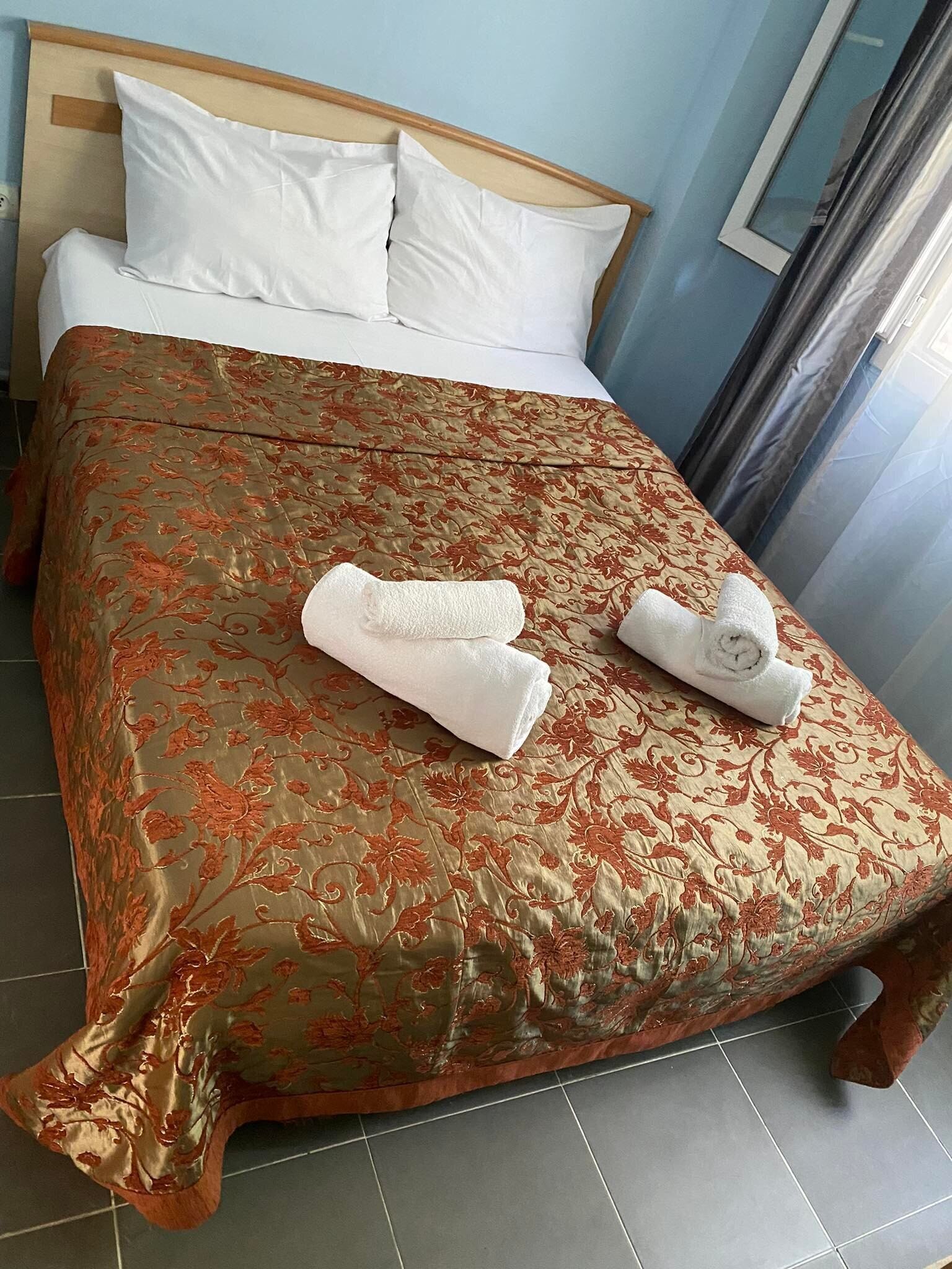 Uma cama bem arrumada com uma colcha floral, dois travesseiros brancos e duas toalhas enroladas sobre a cama.