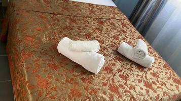 Uma cama bem arrumada com uma colcha floral, dois travesseiros brancos e duas toalhas enroladas sobre a cama.