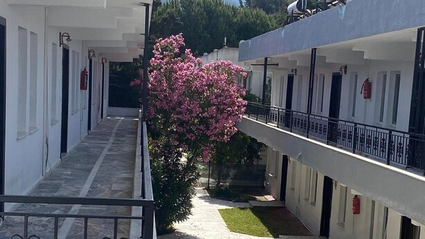 A courtyard with white buildings, a pink flowering tree, and a metal railing. - The Palm Club Apart Otel (Kusadasi)
