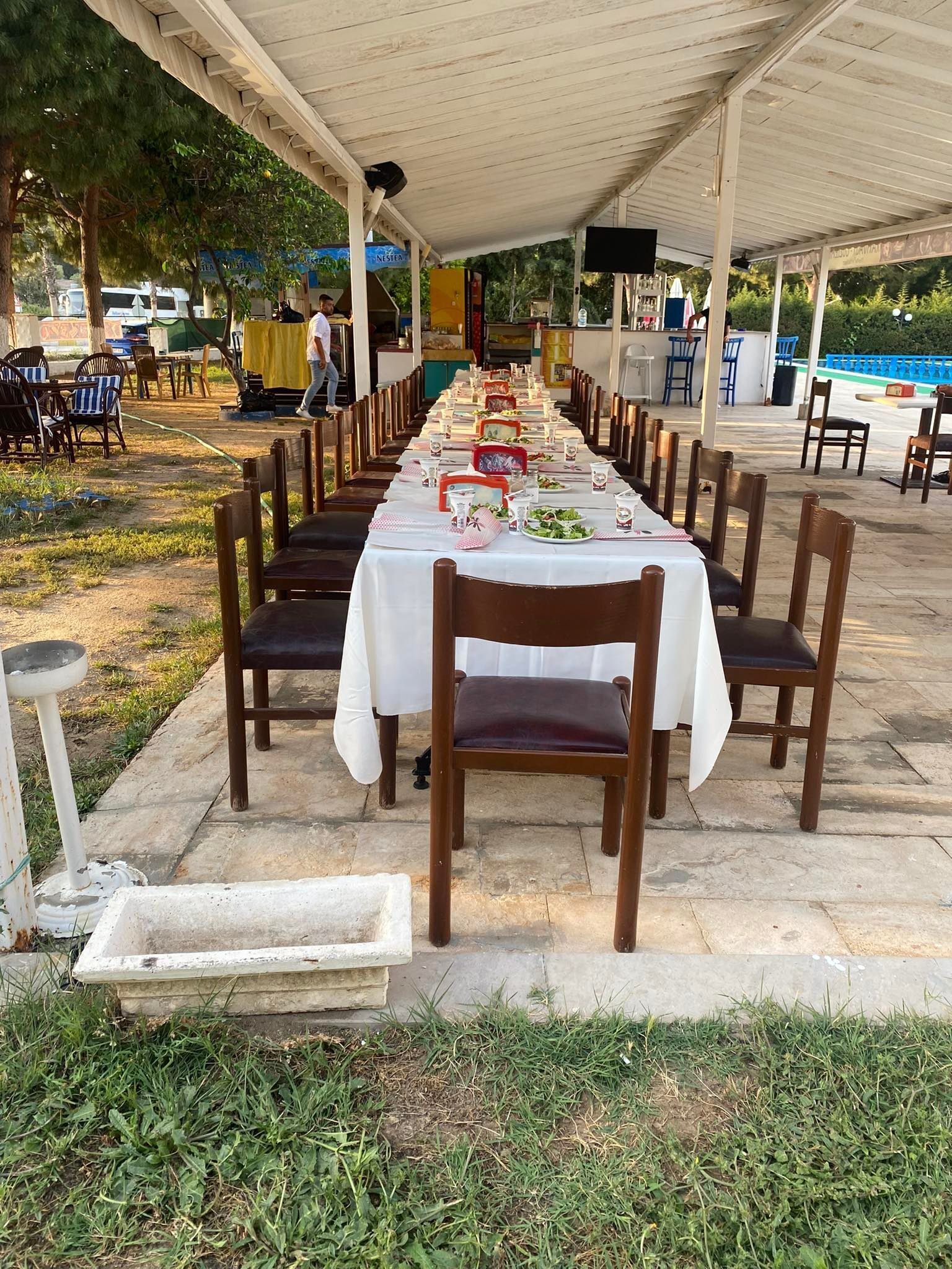 Un'area pranzo all'aperto con un lungo tavolo apparecchiato per un pasto, circondato da sedie.