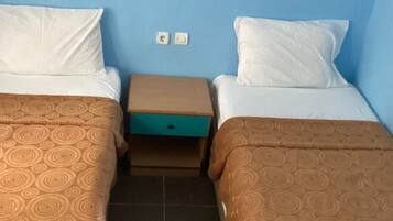 Ein Doppelzimmer mit zwei Betten, jeweils mit einem gemusterten Überwurf, einem kleinen Nachttisch und einer blauen Wand.
