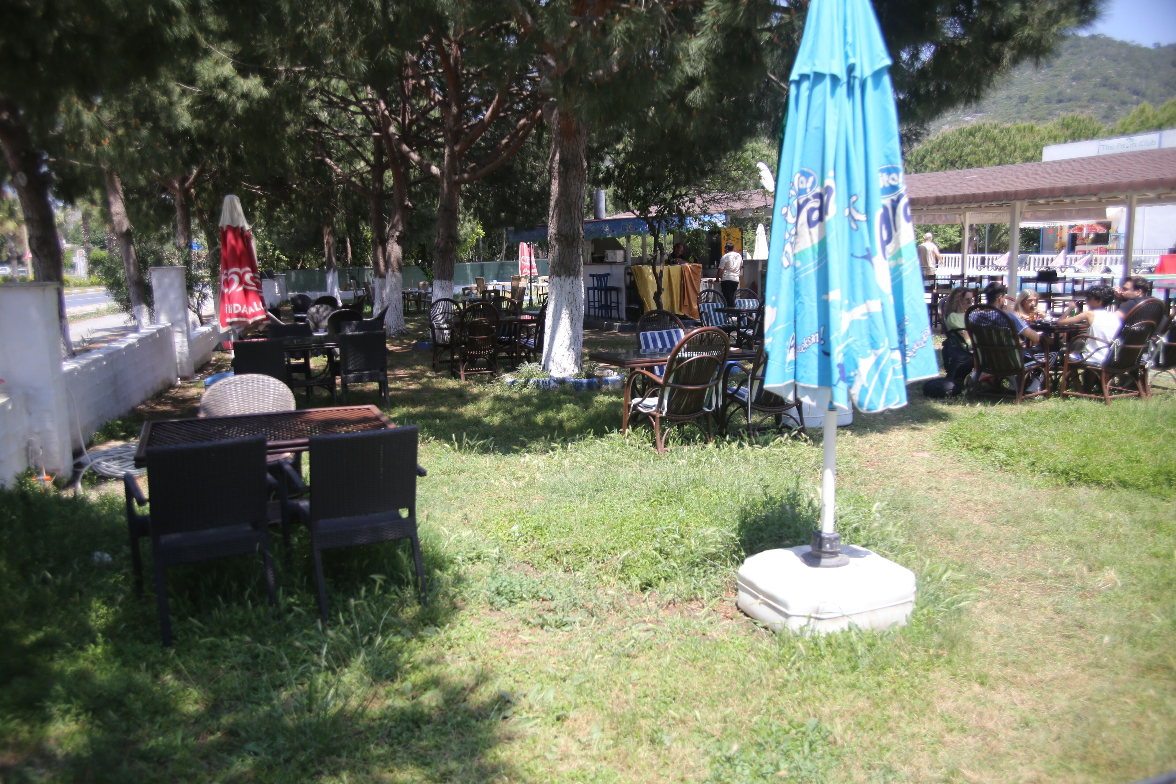 Un espace extérieur aménagé avec des tables et des chaises, dont certaines sont protégées par des parasols, et d’où l’on peut admirer un bâtiment en arrière-plan.