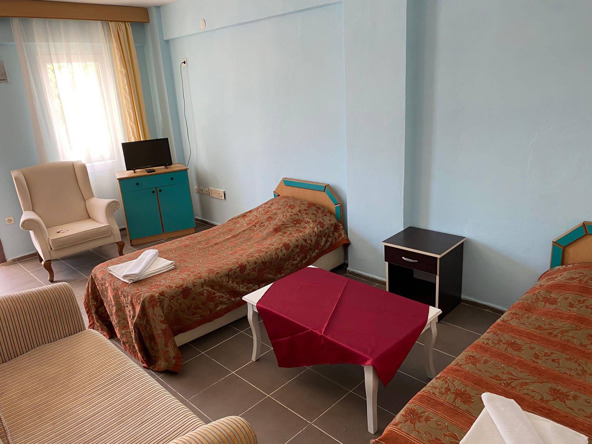 A hotel room with two beds, a chair, a small table, and a TV.