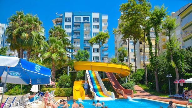A swimming pool with multiple slides, surrounded by palm trees and a building with balconies. - Ark Suite Hotel (Alanya)
