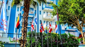 A hotel with a blue and white facade, palm trees, and multiple flags. - Ark Suite Hotel (Alanya)